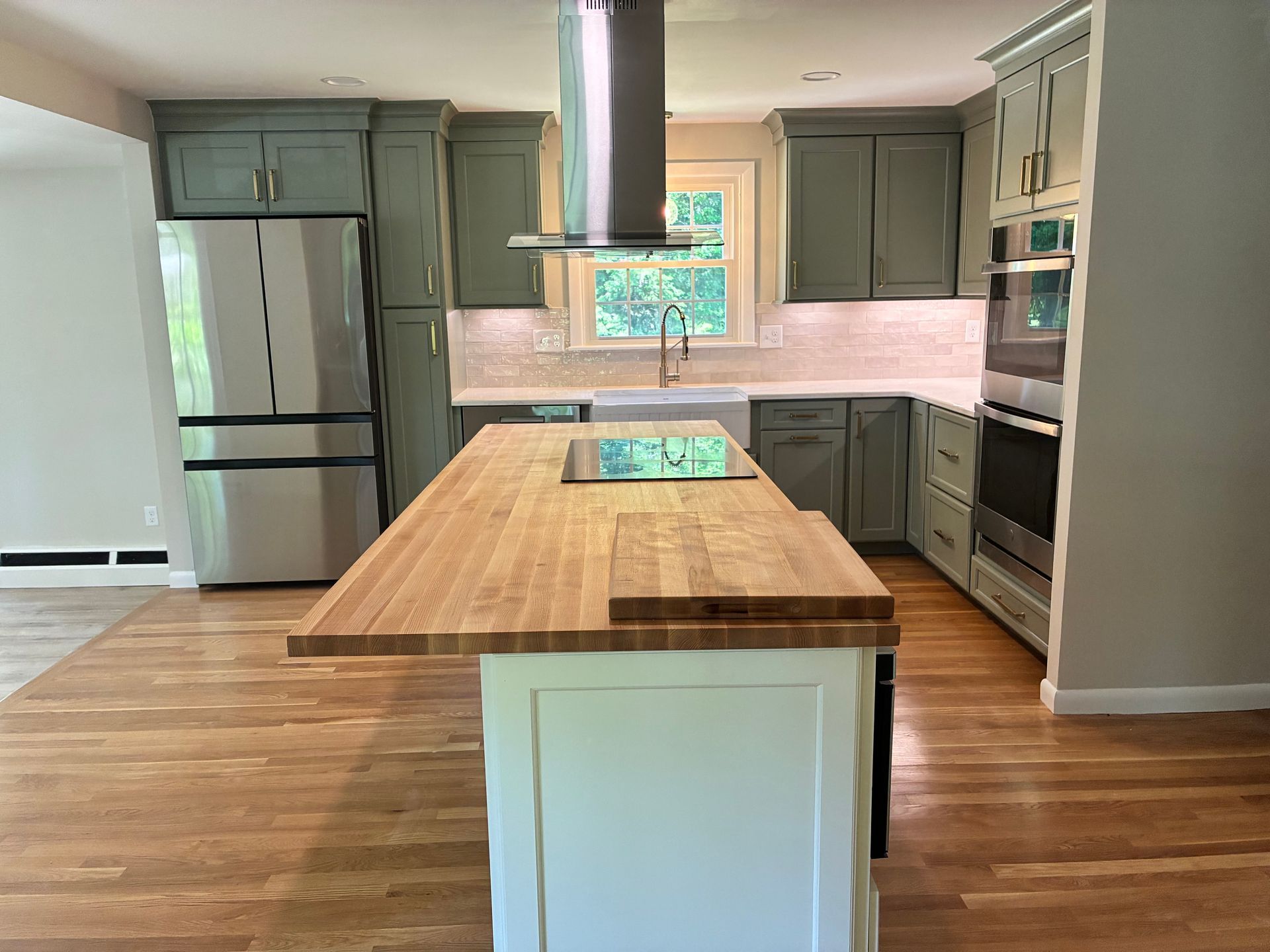 Modern kitchen with green cabinets, stainless fridge, and large wooden island on hardwood floors