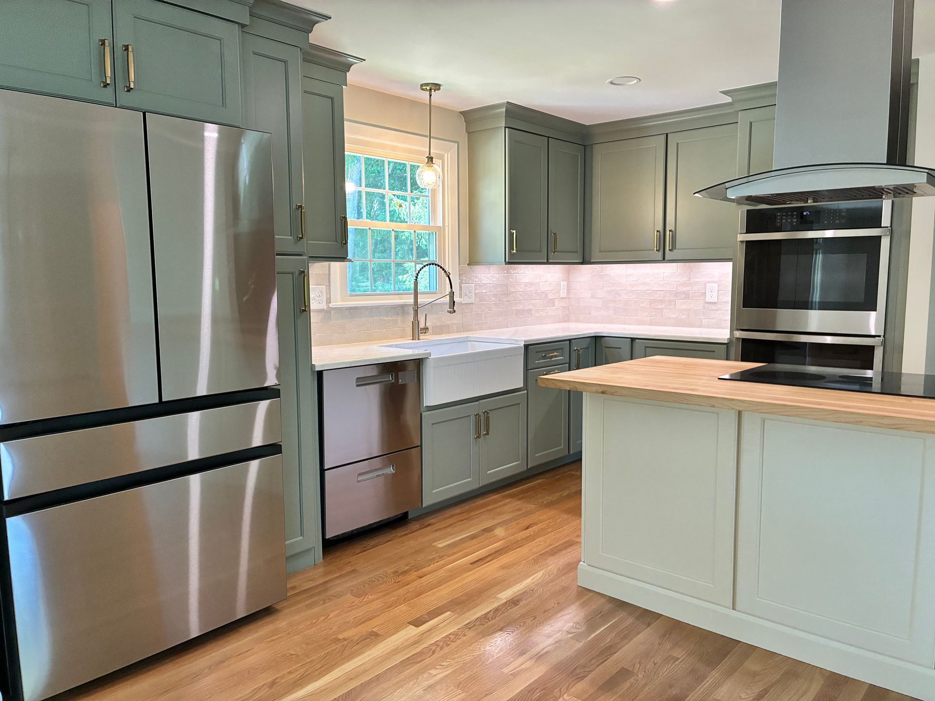 Bright kitchen with stainless steel appliances, sage cabinets, white countertops, and wood floors