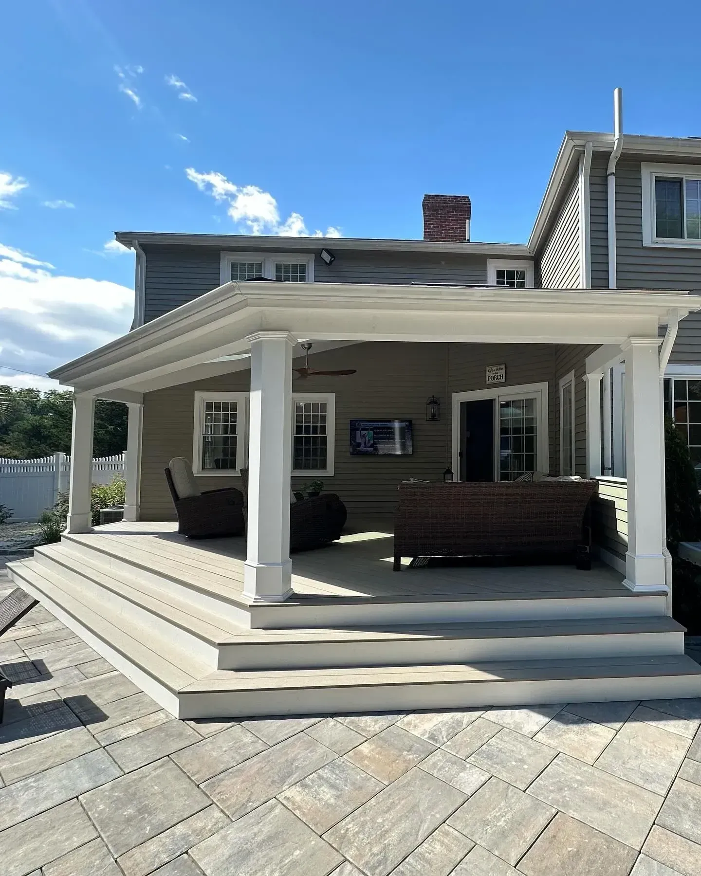 Covered outdoor patio with a seating area, overlooking a stone patio and house.