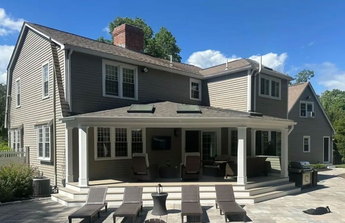 Two-story house with a covered patio and steps leading to a stone patio with lounge chairs.