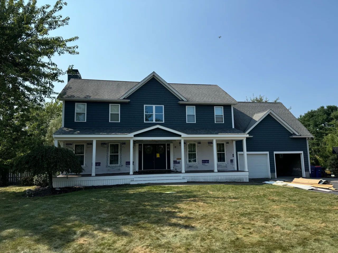 Two-story house with dark blue siding, white trim, porch, and a garage on a sunny day.