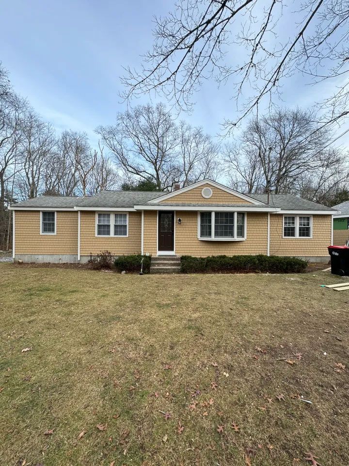 Tan ranch-style house with dark door, small porch, and yard; cloudy sky above.