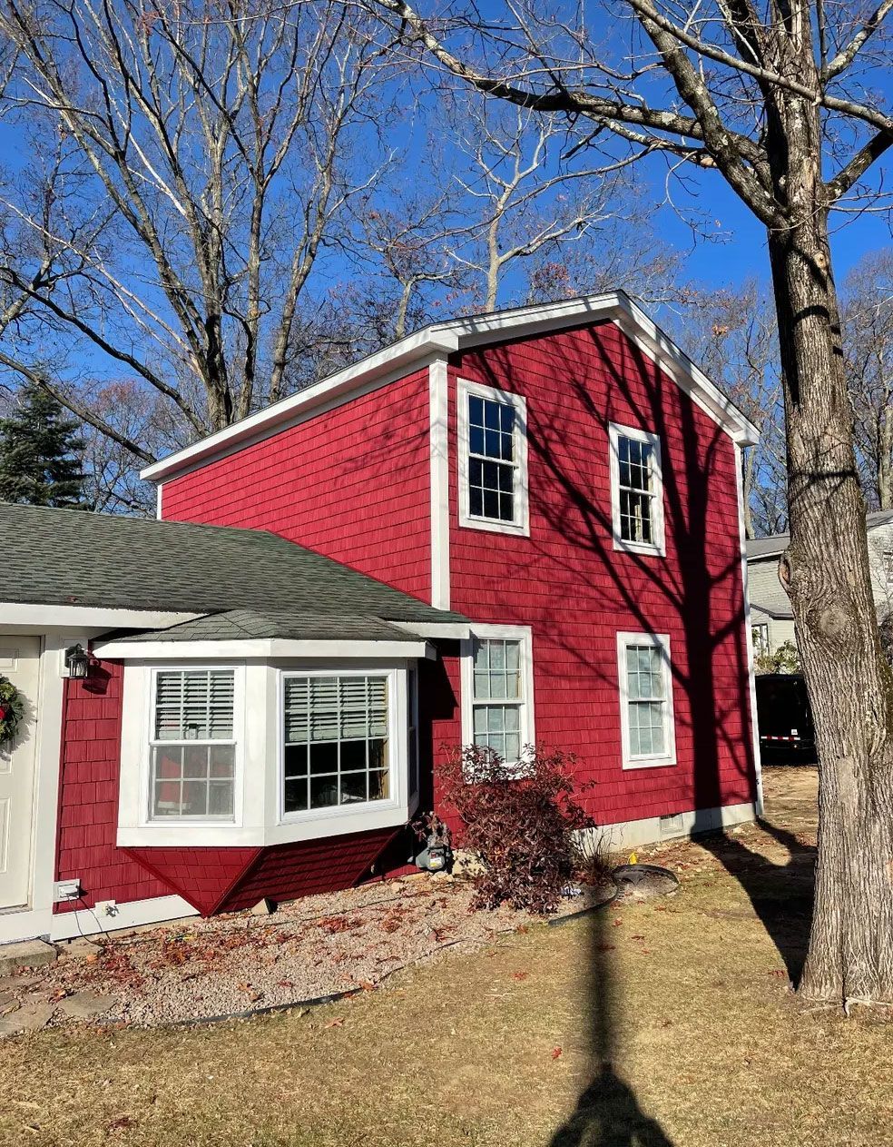 Red house with white trim, green roof, and bare trees under a blue sky.
