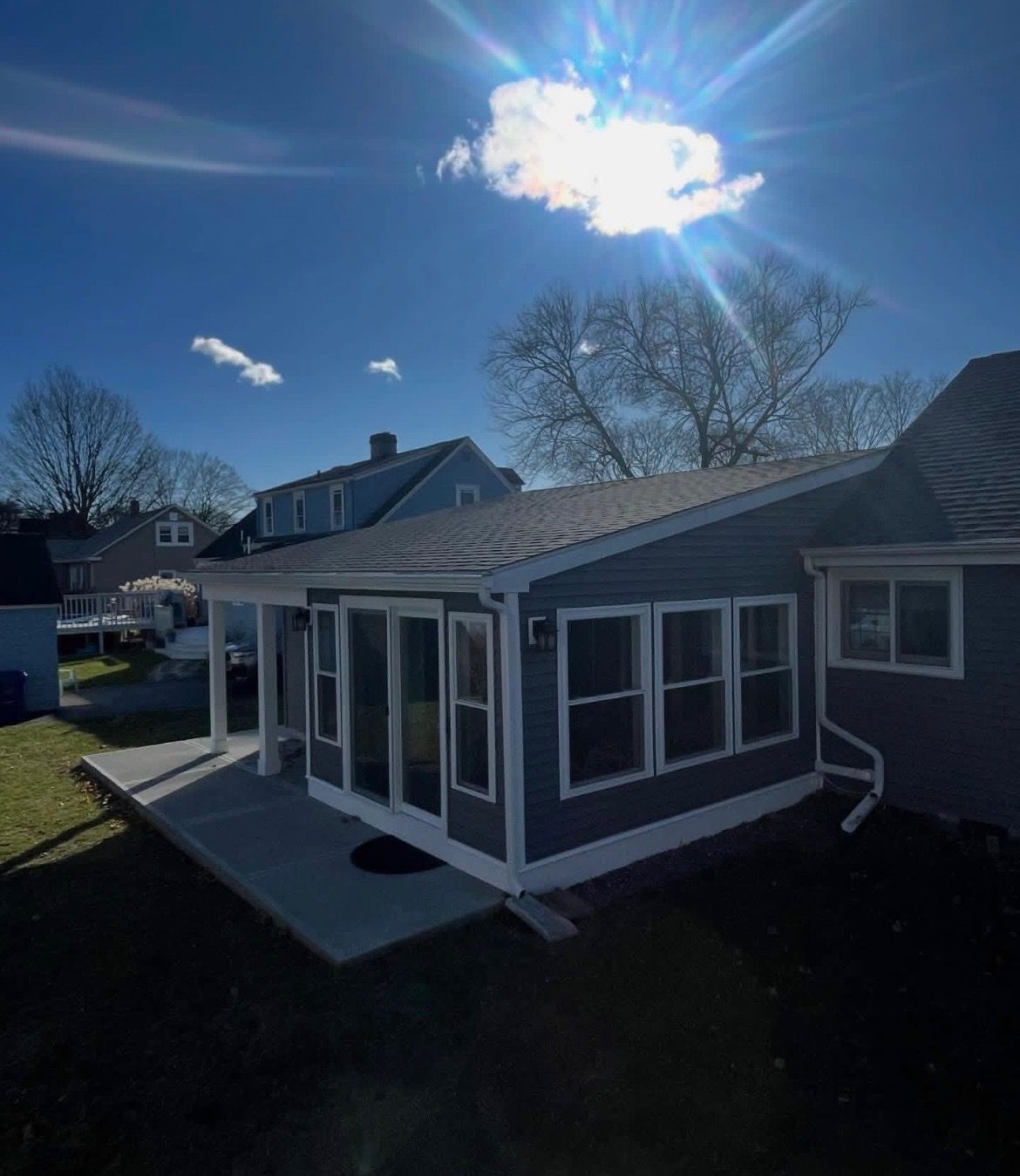 Sunlit backyard view of a gray house addition with screened porch and white-trim windows