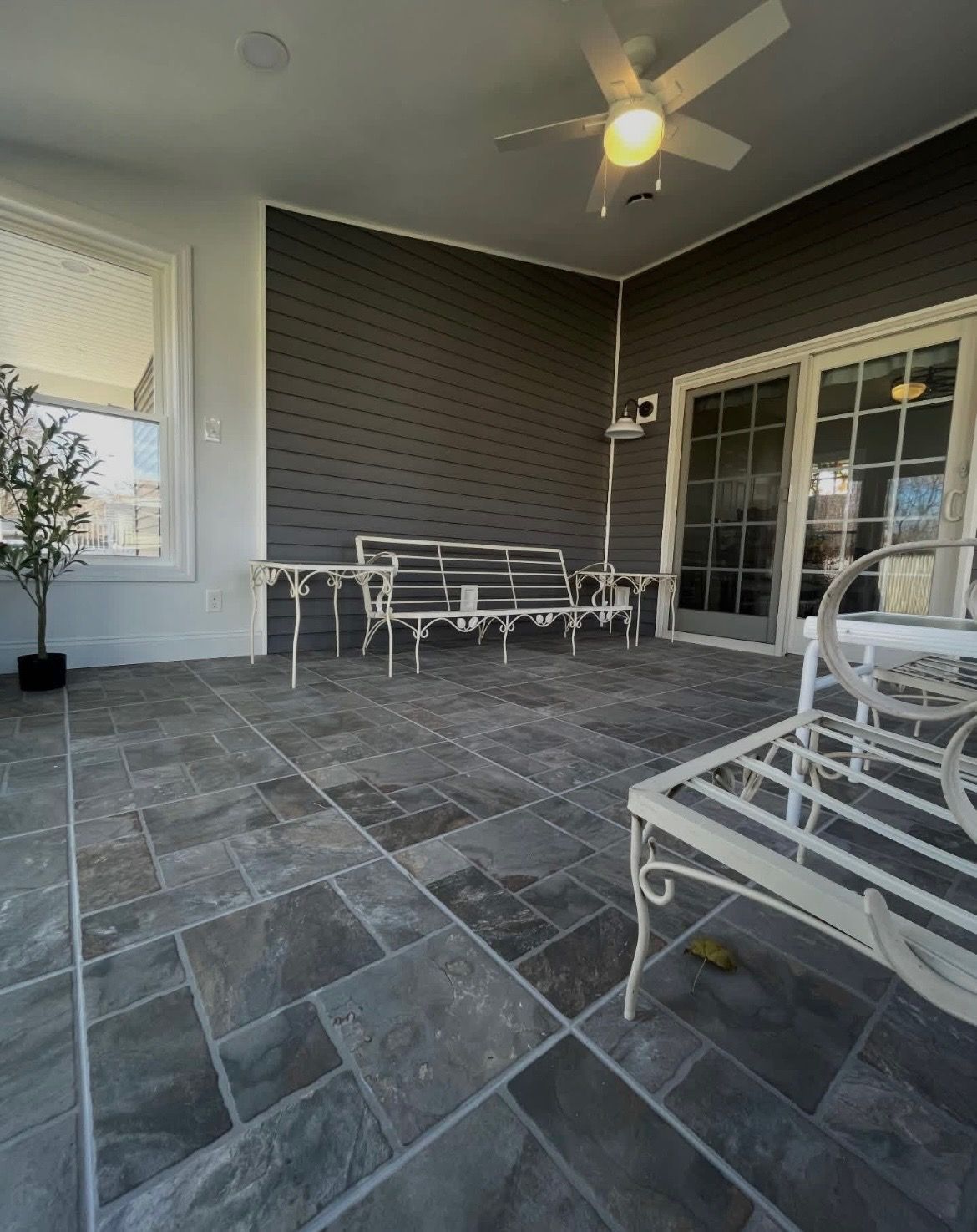 Covered patio with gray tile floor, white metal chairs, dark wall, and sliding glass door
