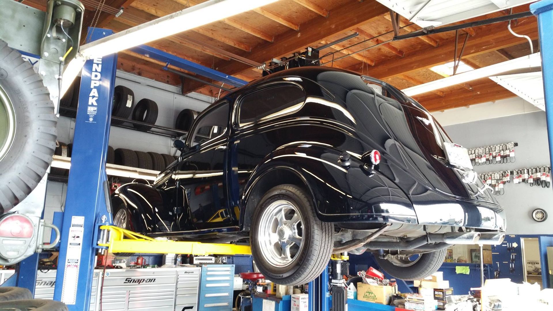 A shiny black vintage car lifted on a blue and yellow hydraulic auto repair shop lift.