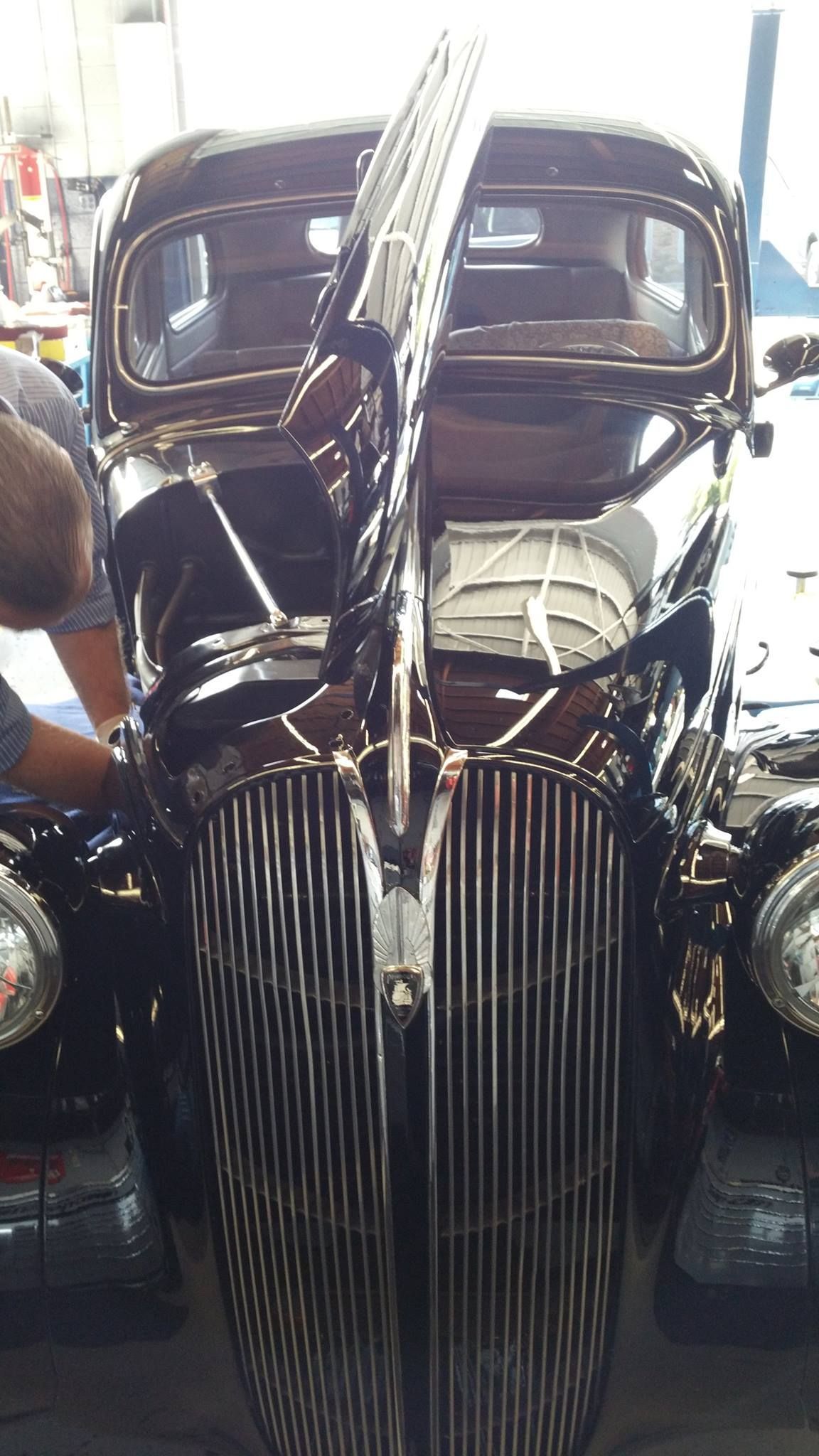 A dark vintage car with a vertical, chrome-accented grille and an open hood, parked inside a garage.