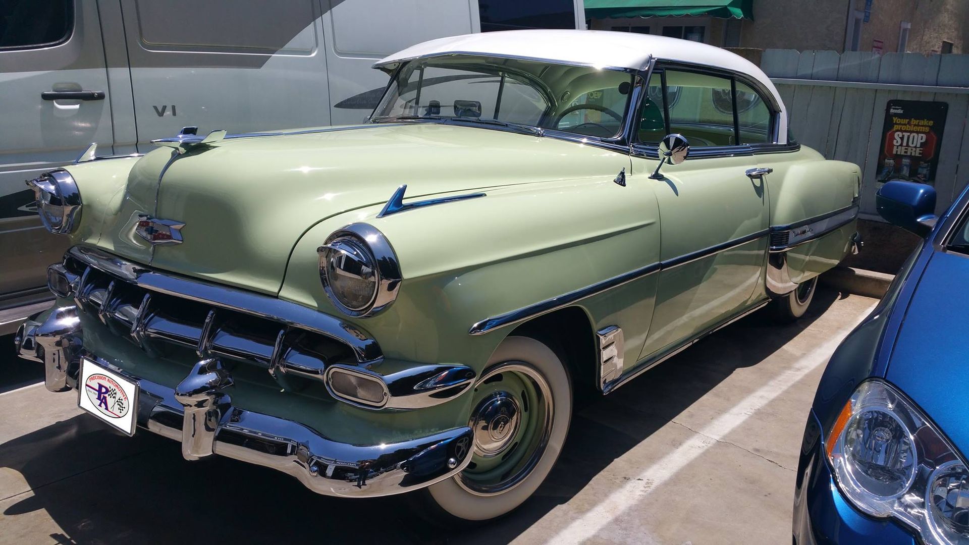 A pale green and white classic Chevrolet Bel Air coupe parked in a parking lot on a sunny day.