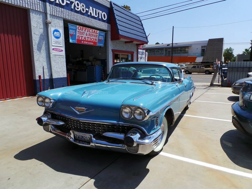 A vintage light blue Cadillac parked in front of an automotive repair shop on a sunny day.