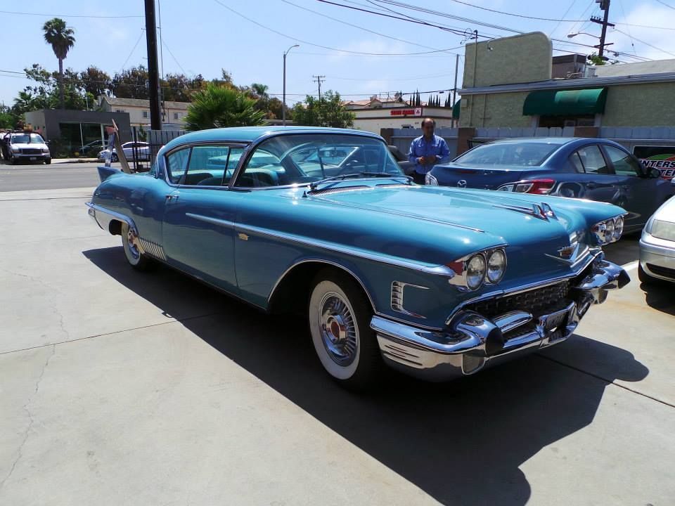 A vintage blue Cadillac with chrome trim and whitewall tires parked on a paved lot in daylight.