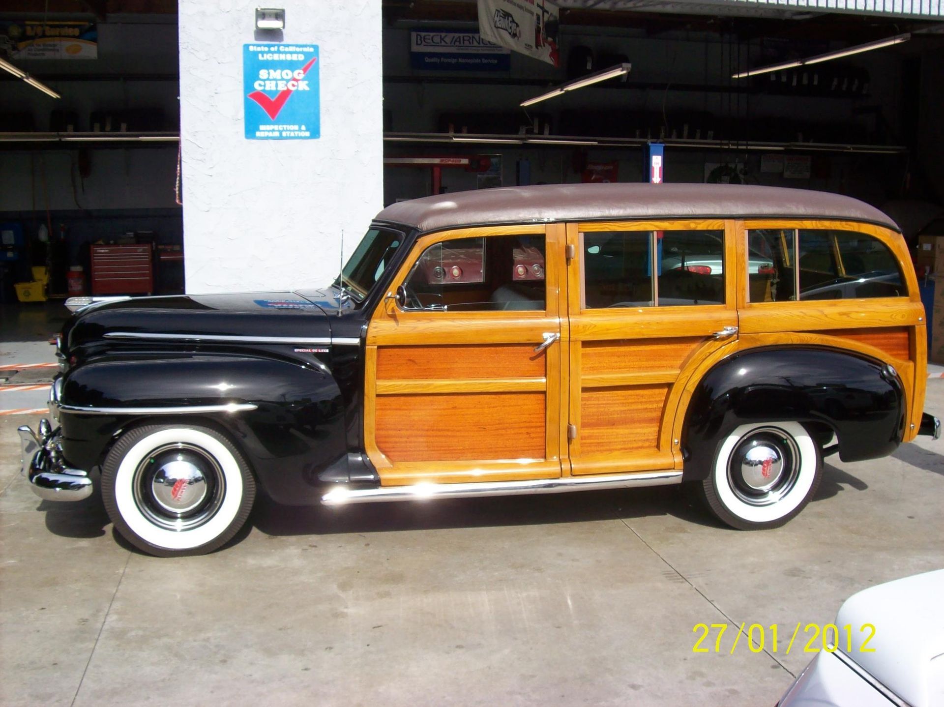 A classic black station wagon with wood-paneled sides and whitewall tires parked in an indoor garage.