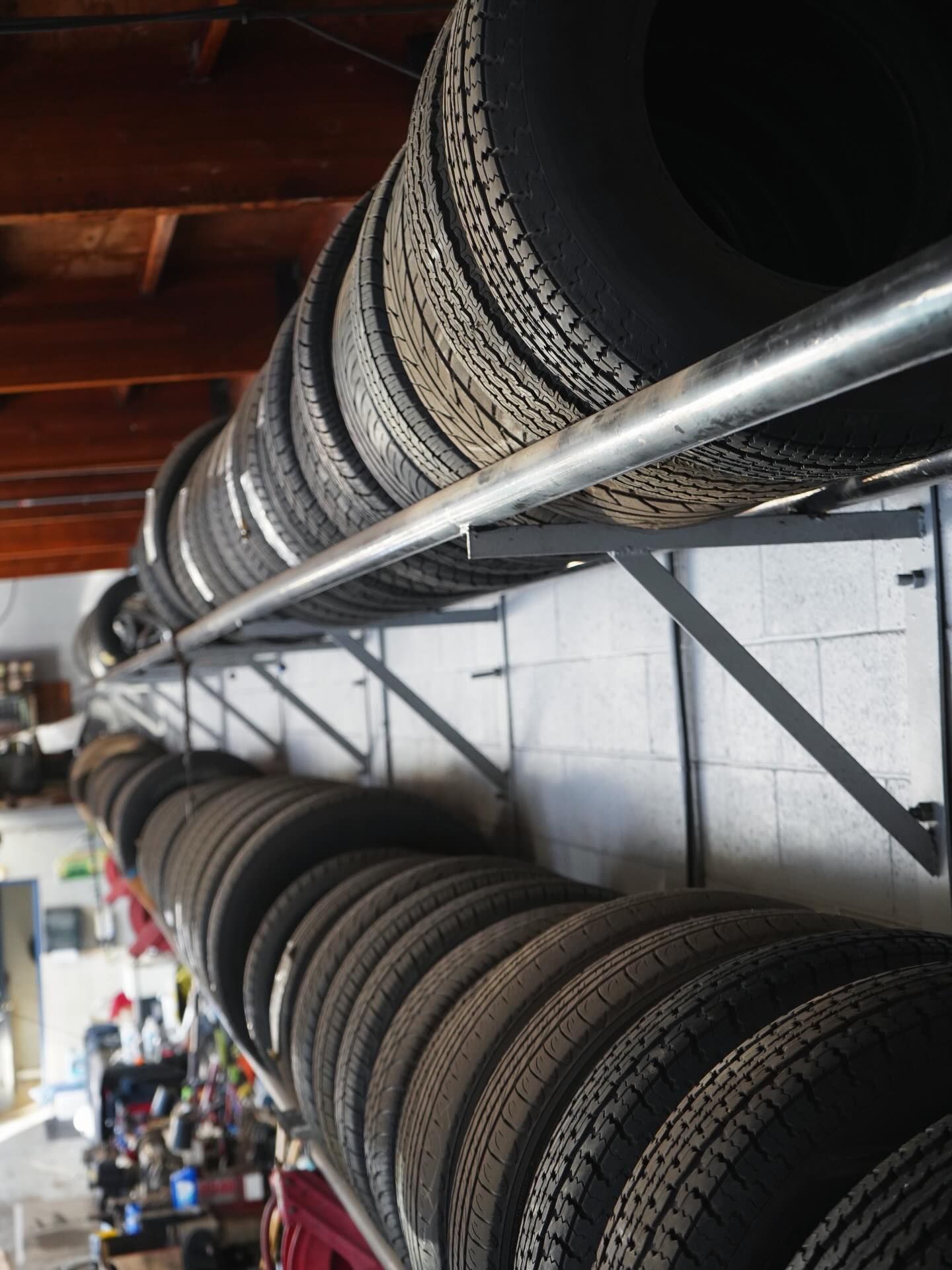 Two metal wall-mounted racks are stacked with rows of black car tires in a workshop or garage.