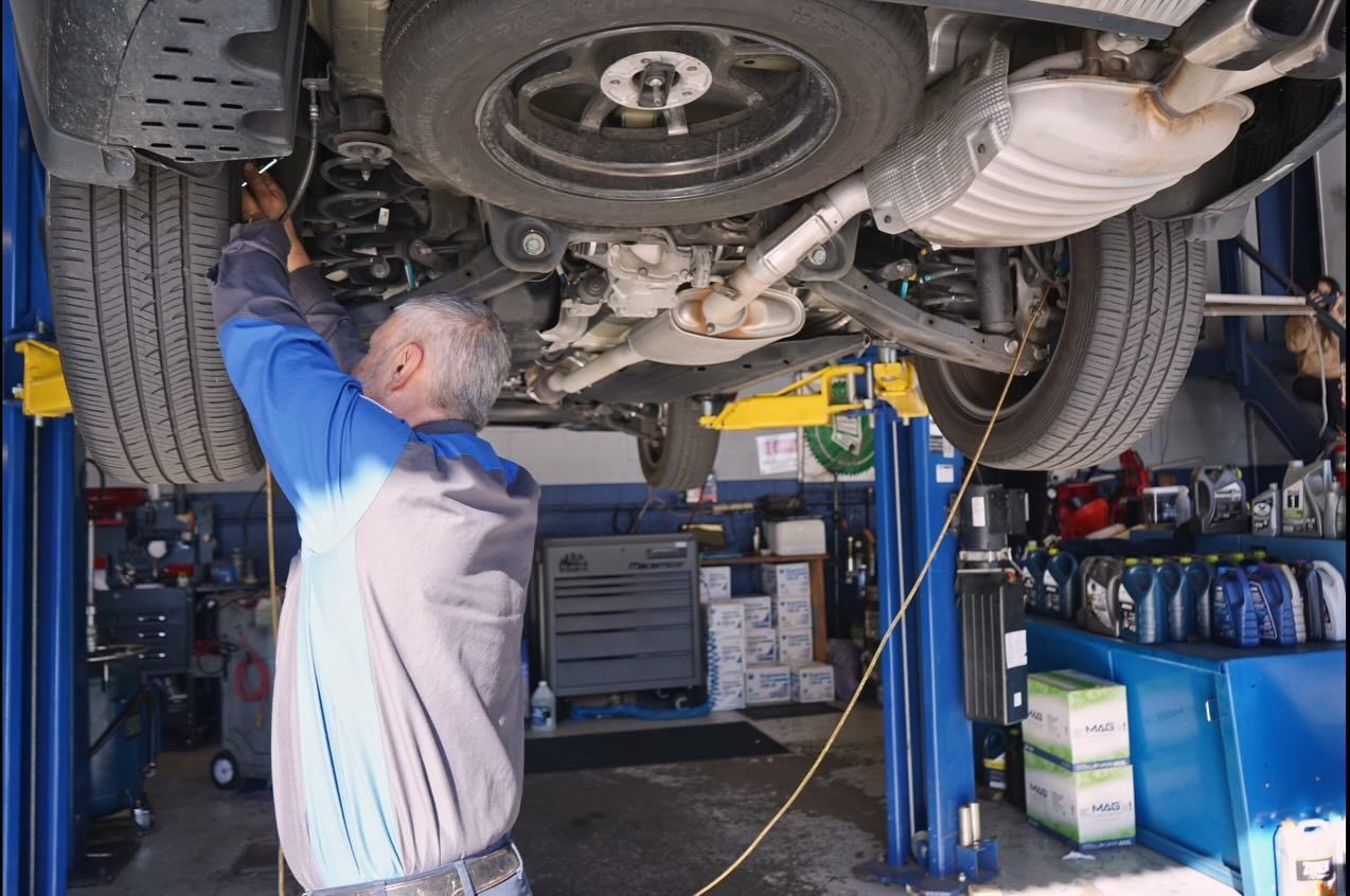 A mechanic working on the undercarriage of a vehicle raised on a lift in an auto repair shop.