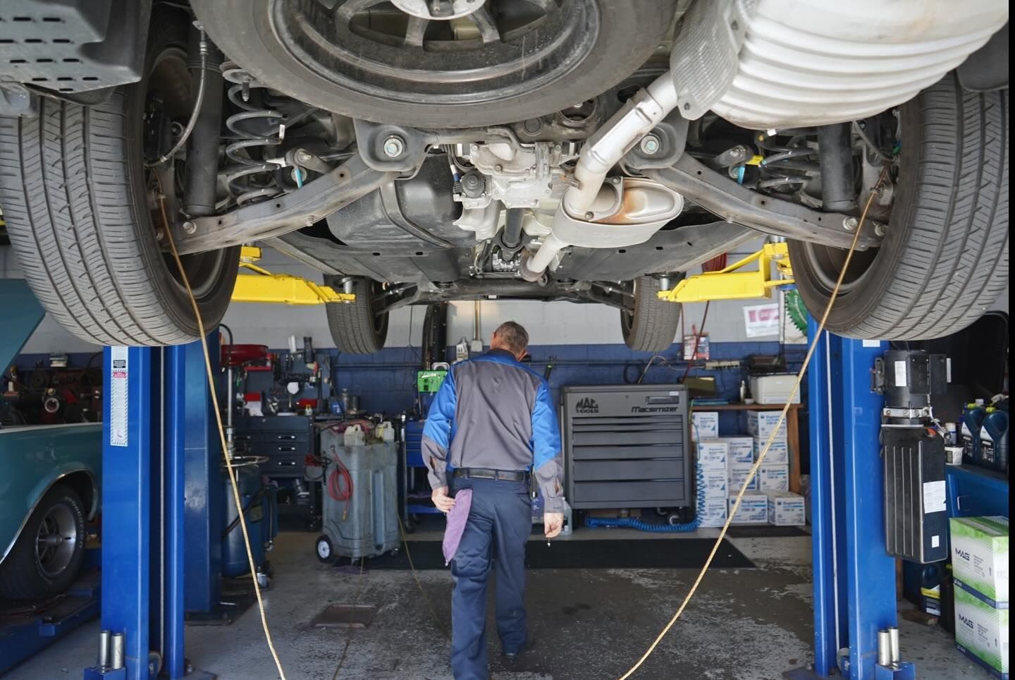 A technician works under a vehicle raised on a car lift inside an automotive repair shop.