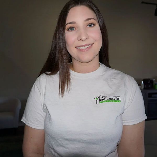 Woman with long brown hair smiles wearing a white t-shirt with a green logo indoors.