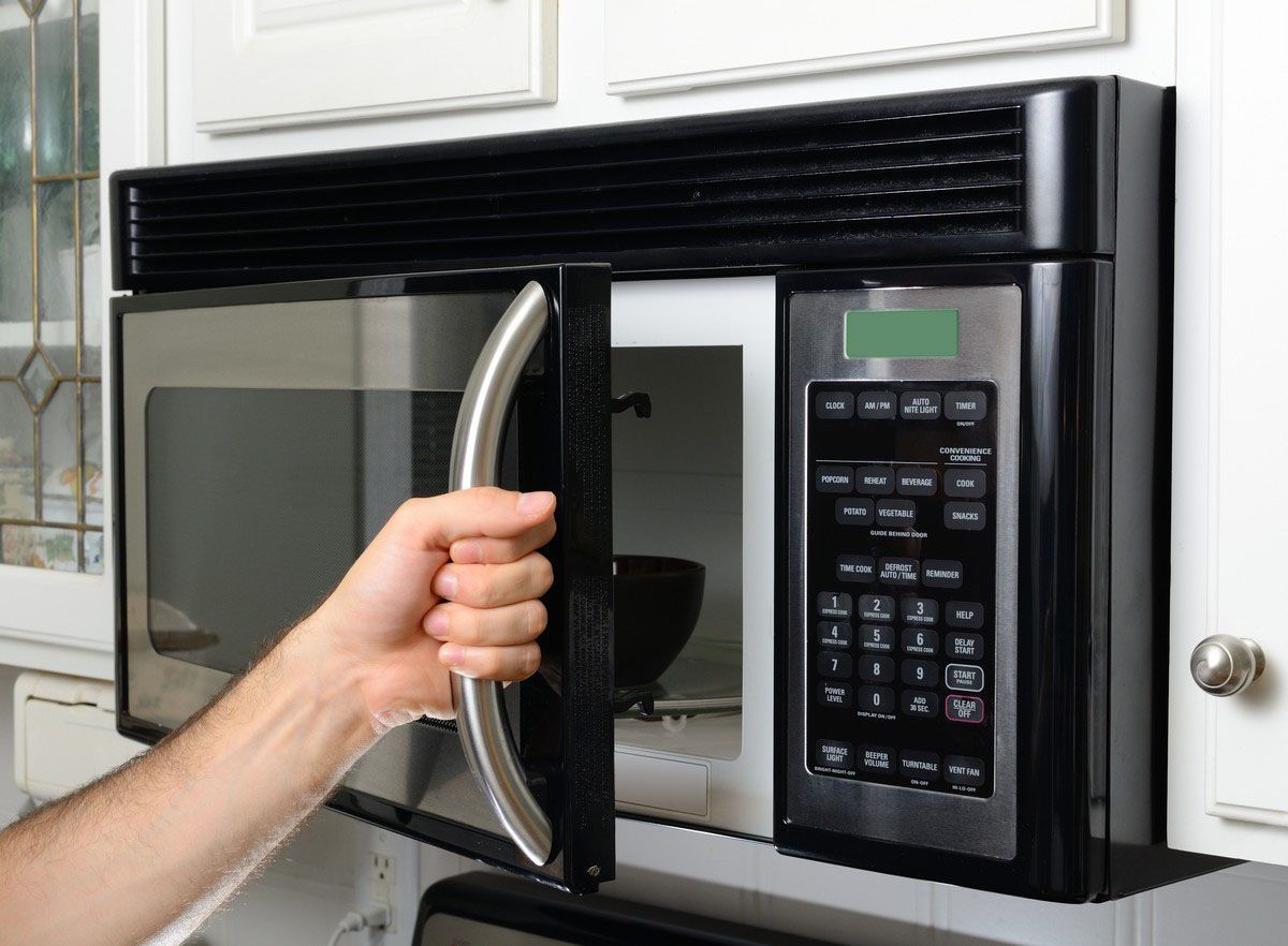 Hand opening a black and silver microwave in a kitchen.