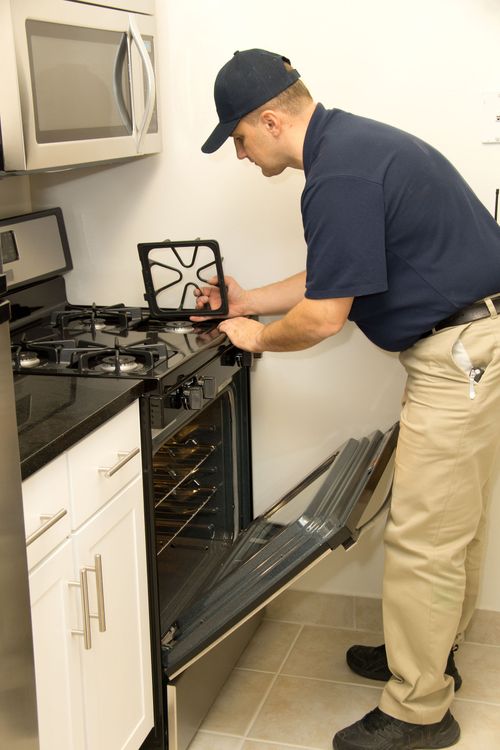 Man in uniform inspecting a stove in a kitchen. He is holding a burner grate.
