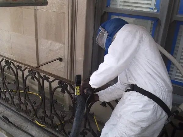 A man in a white suit is working on a wrought iron railing.
