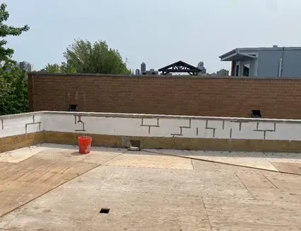 Rooftop with a brick wall, red bucket, and concrete surface on a sunny day.