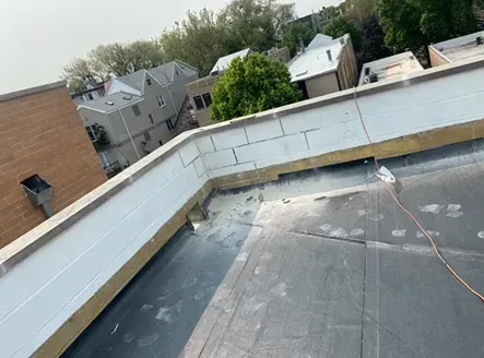Rooftop view of a commercial building. Features flat roofing and a white brick wall. Surrounding buildings and sky visible.