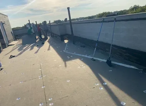 Workers on a flat roof. They are installing new roofing material, and it is a sunny day.
