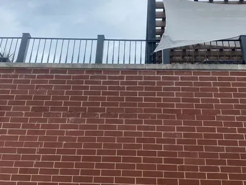 Red brick wall with a black railing on top, partial view of a white canopy and cloudy sky.