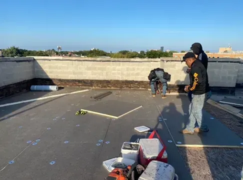 Construction workers on a flat roof, installing roofing materials.