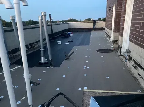Rooftop construction: partially completed dark roofing material, vents, and white wall.