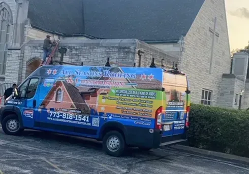 Van with roofing business logo parked near a church with workers on the roof.