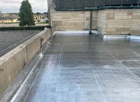 Flat roof with metal flashing and concrete wall. Building in background.