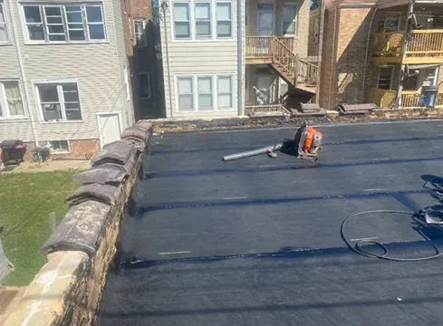 Flat roof with black surface, brick border, and tools, likely for repair, are visible.