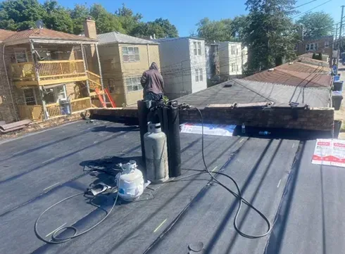 Roofer on a flat roof with propane tanks, working on a building in a neighborhood.