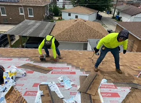 Two roofers in neon shirts working on a rooftop, cutting shingles. Sunny, residential setting.