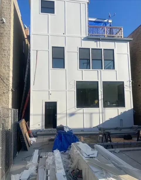 White modern building exterior with large windows, construction materials on the ground.