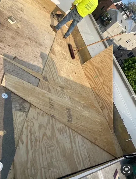 Person on a roof installing plywood sheets. Construction site in daylight.