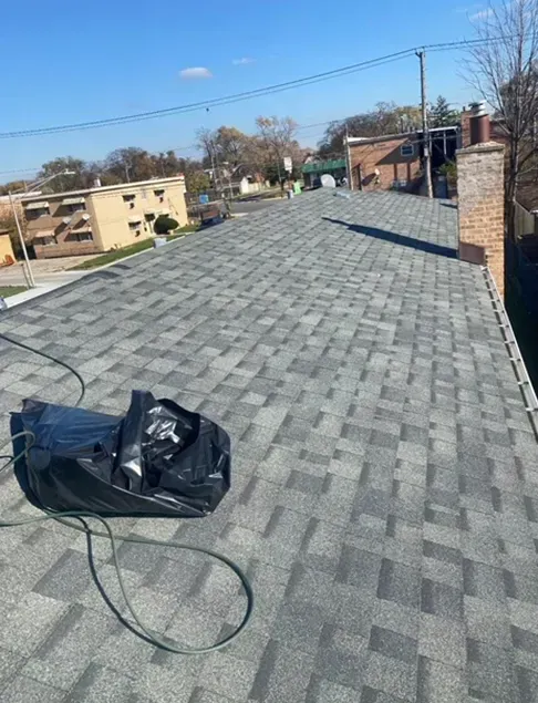 Newly shingled gray roof with a black bag and a brick chimney in the background on a sunny day.