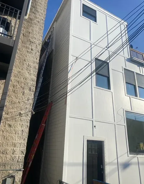 White building exterior with windows, door, and ladder propped against the side, power lines.