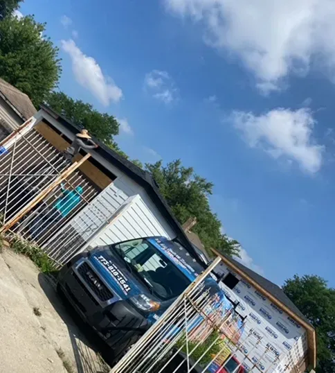 Blue van parked in a driveway next to a building, with a cloudy blue sky in the background.
