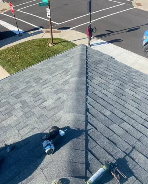 View from a roof of a gray shingle roof, tools in foreground, street and pedestrian in background.