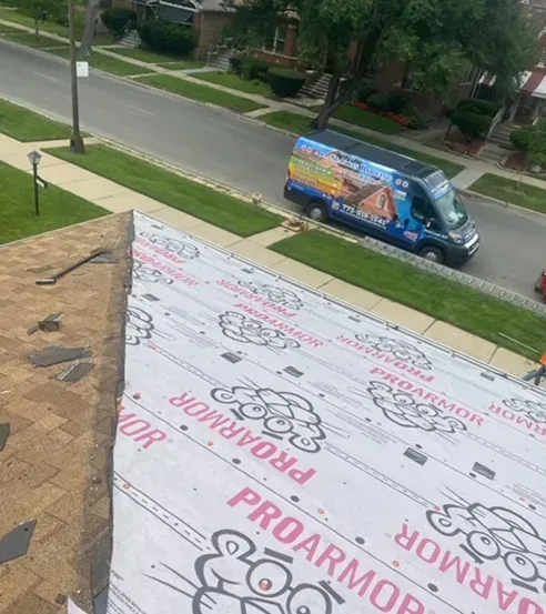 Roofing work: Installing underlayment on a roof with a work van parked on the street.