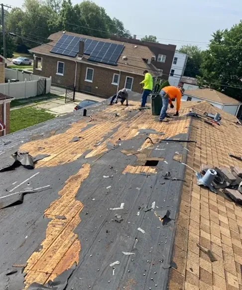 Roofers removing old shingles from a house with solar panels in a residential neighborhood.