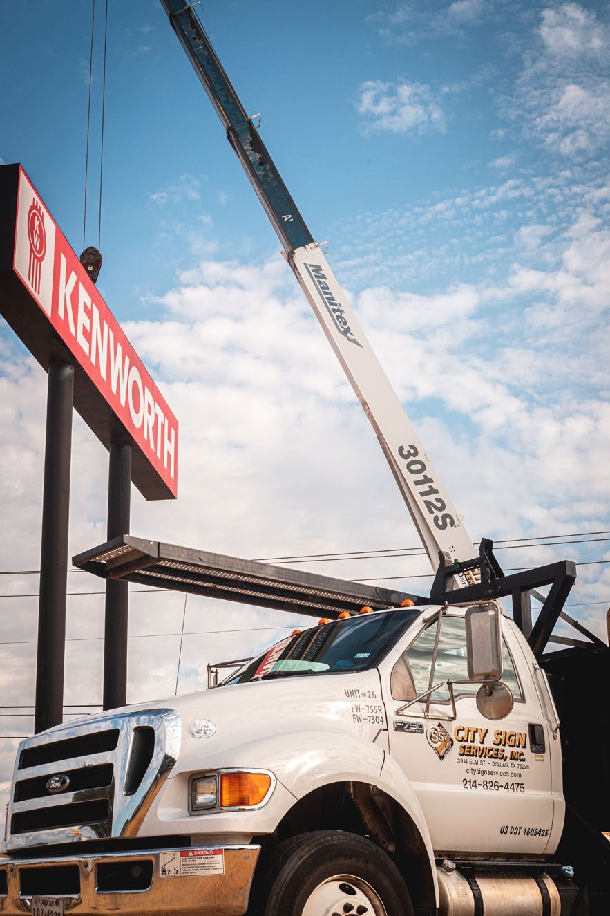 A white truck with a crane attached to it is parked in front of a sign