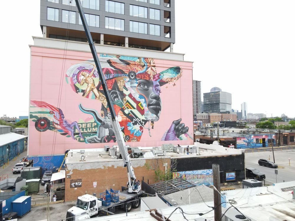 A large mural is being painted on the side of a building.