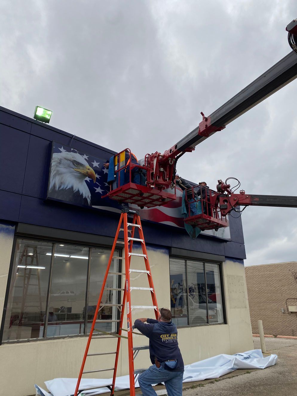 A man on a ladder is working on a sign on the side of a building