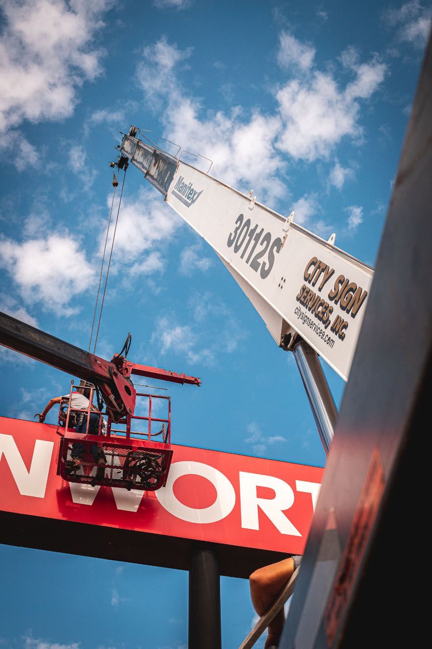 A crane is lifting a large red and white sign.