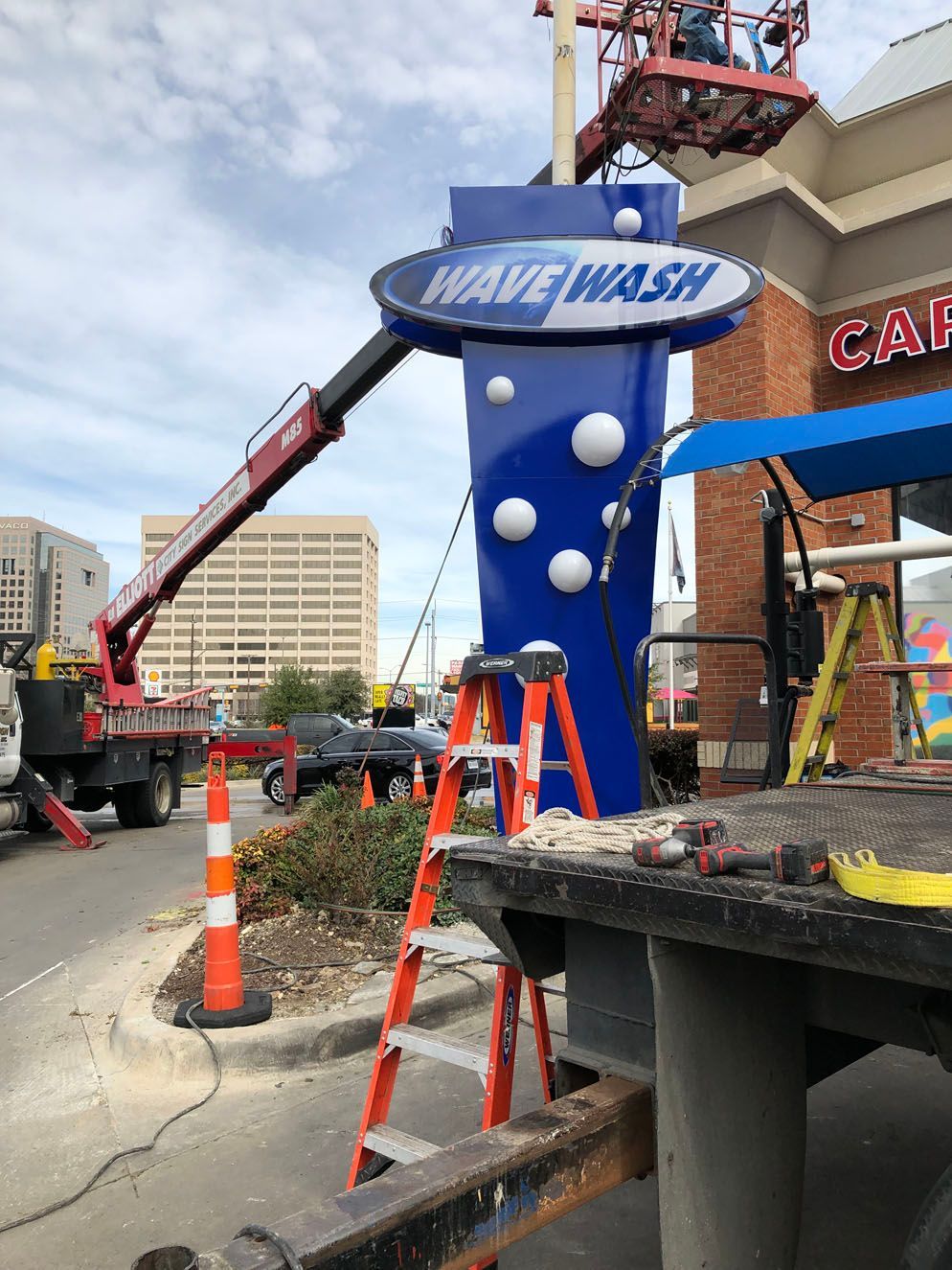 A wave wash sign is being installed in front of a car wash