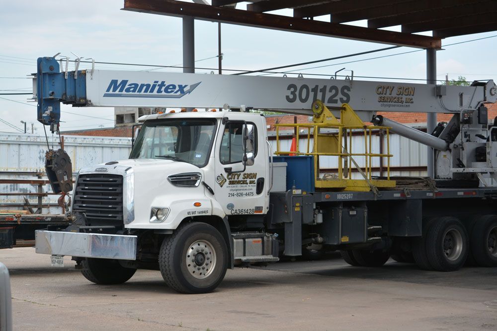 A white truck with a crane on the back is parked under a roof