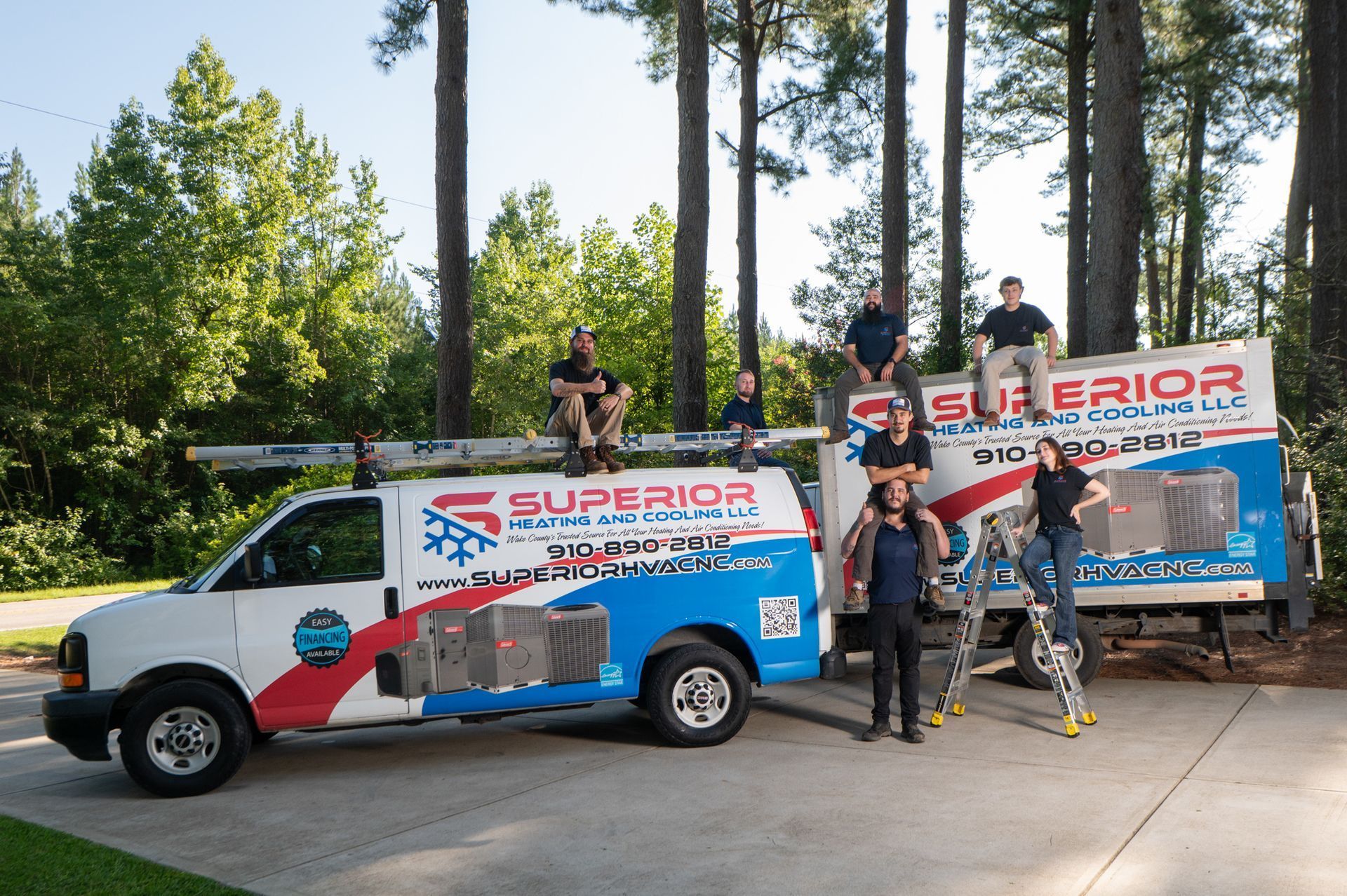 Two Superior Plumbing trucks with a crew posing outdoors by tall trees and a driveway.