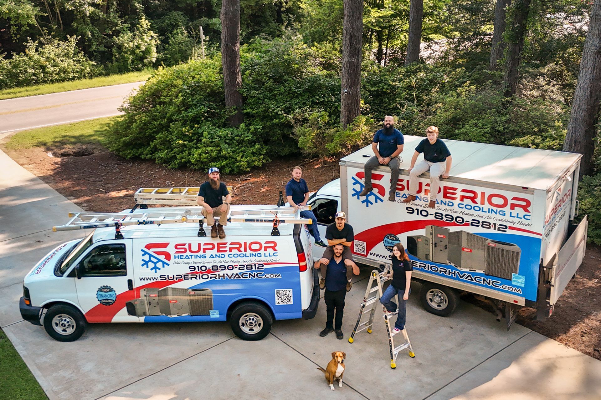 Team with white and blue Superior trailers and van parked in a driveway, holding banners.