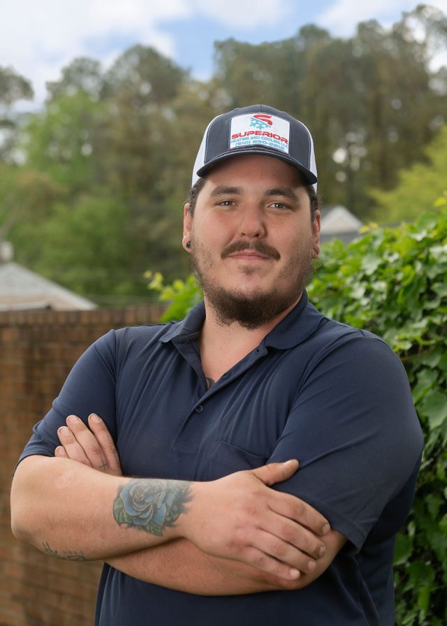 Man with crossed arms, wearing a navy polo shirt and baseball cap, smiling, outdoors.